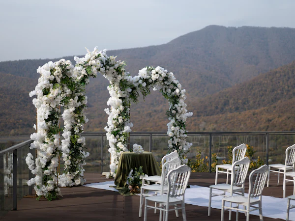 Arco de flores blancas y sillas listas para una ceremonia al aire libre frente a las montañas