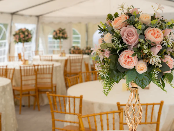 Salón decorado con mesas redondas, sillas doradas y centros de mesa de rosas